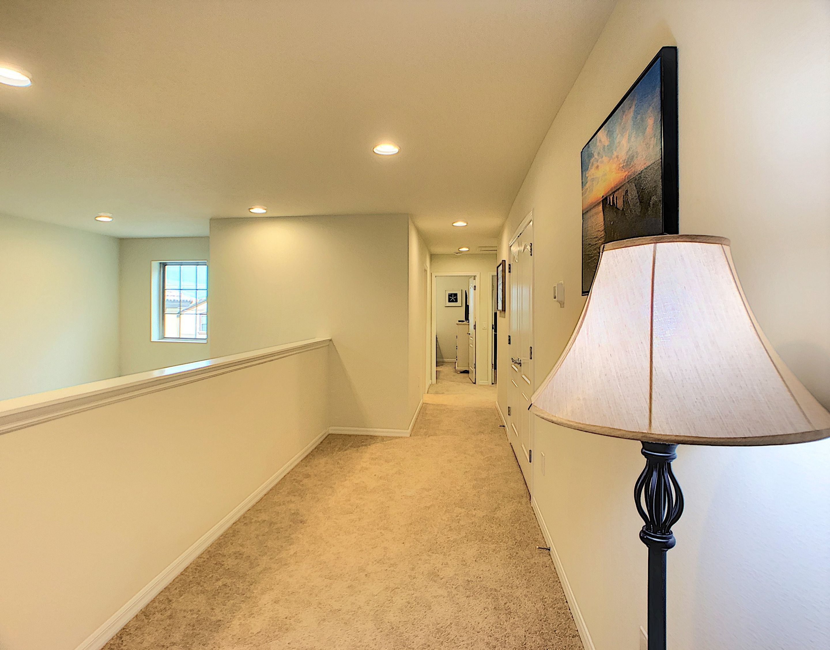 A hallway with a carpeted floor, a wall-mounted lamp, and a framed picture.