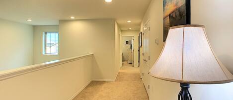 A hallway with a carpeted floor, a wall-mounted lamp, and a framed picture.