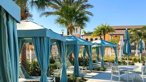 A poolside area with blue canopies, lounge chairs, and a tiled walkway. - Tropical Sunset by Florida Spirit (Kissimmee)