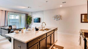 A modern kitchen with a large island, dark cabinetry, and a flat-screen TV mounted on the wall. - Tropical Sunset by Florida Spirit (Kissimmee)