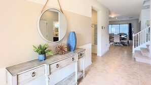 A spacious living area with a large mirror, a wooden console table with decorative items, and a view into a dining area with a staircase. - Bengal Sunrise by Florida Spirit (Kissimmee)