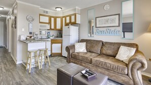 A compact living space with a kitchenette, a brown leather sofa, and a small bar stool area. - Casa Del Mar Beach Suites (Galveston)