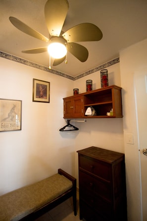 Um quarto com ventilador de teto, um banco, um armário de madeira e um quadro na parede.