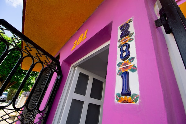 Um edifício com fachada rosa, um portão de metal preto e uma placa colorida com o número 281.