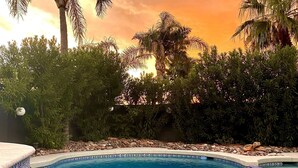 A swimming pool with clear blue water, surrounded by lush greenery and palm trees, under a sunset sky. - 9 AM check in 9 PM check out, south facing sunny yard, Kierland area, 6 bikes (Scottsdale)