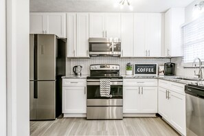 Une cuisine moderne avec des armoires blanches, des appareils en acier inoxydable et un dosseret de carrelage disposé en motif chevron.