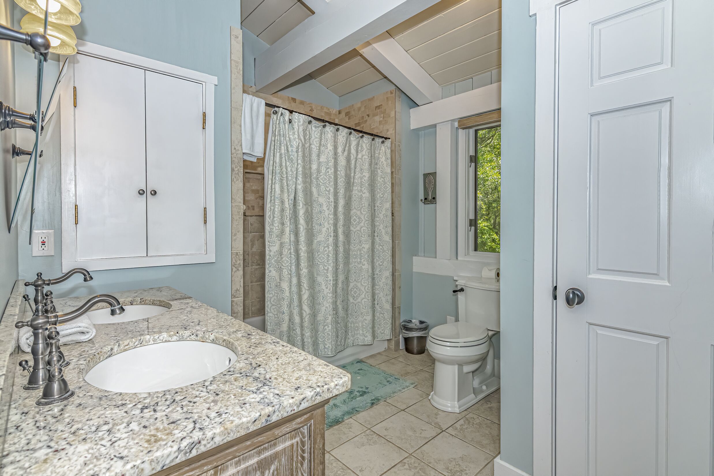 Une salle de bain avec un lavabo blanc, un meuble-lavabo et une douche dotée d’un rideau à motifs.