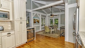 Una cocina amplia con muebles blancos, piso de madera y un comedor con sillas de mimbre.