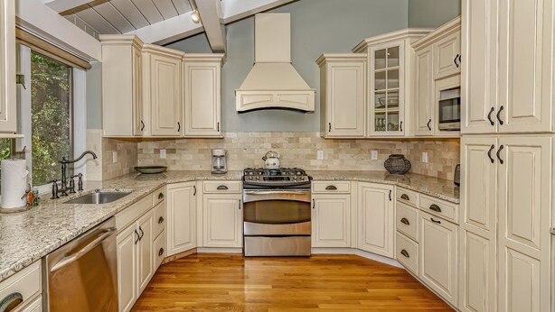 Una cocina con armarios blancos, una estufa de acero inoxidable y piso de madera.