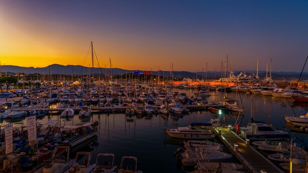 Ein Hafen im Abendlicht mit zahlreichen Booten an den Liegen, einer Holzsteg und Bergen in der Ferne.