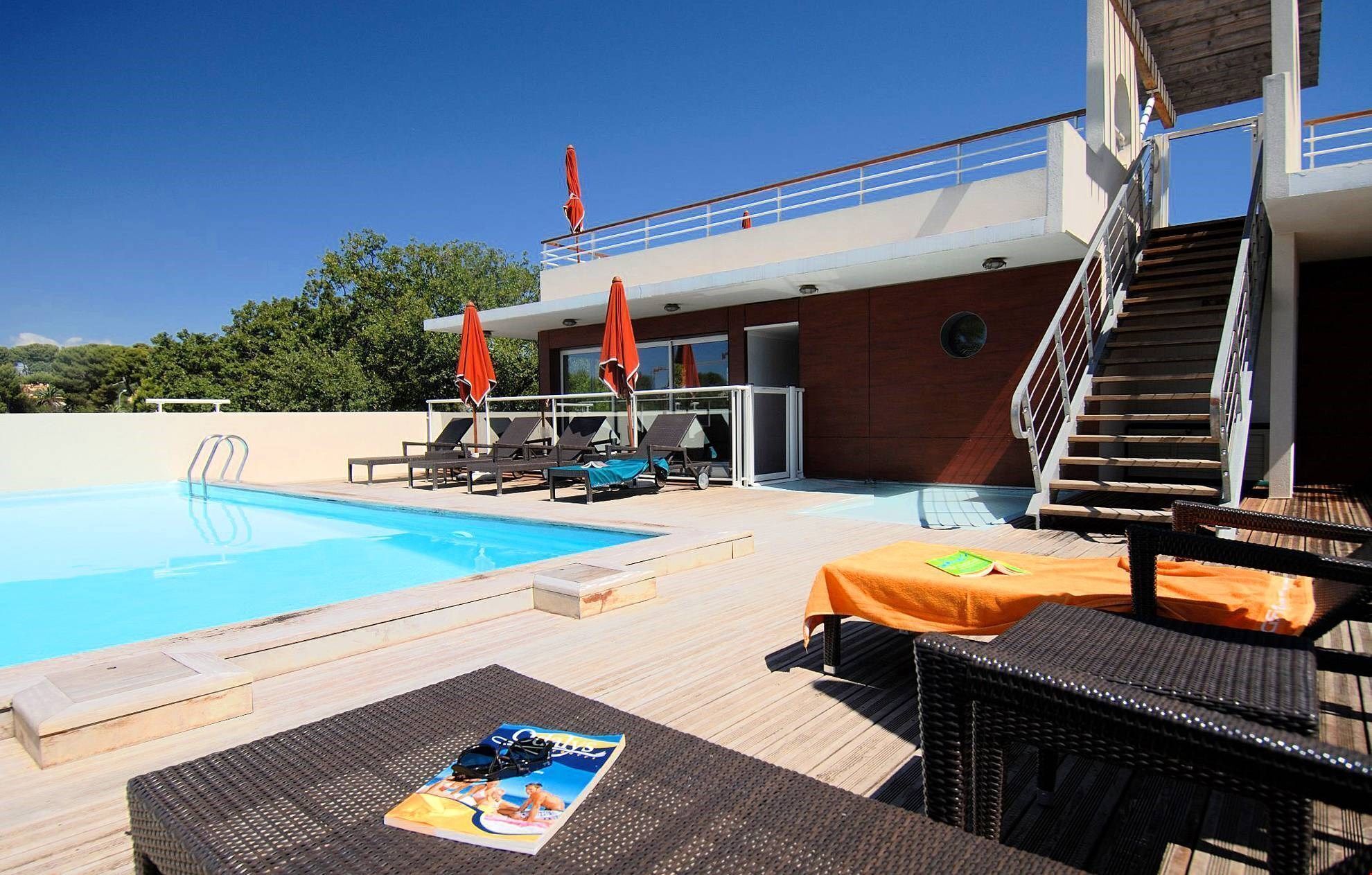 A pool area with lounge chairs and umbrellas, a wooden deck, and a staircase leading to an upper level.