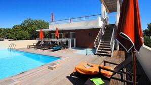 Ein Poolbereich mit Holzterrasse, Liegestühlen und orangefarbenen Sonnenschirmen.