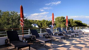Eine Terrasse mit Liegestühlen und roten Sonnenschirmen mit Blick auf ein Gewässer und viel Grün.