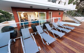 A deck with sun loungers, a glass balustrade, and a view of the interior. - Appart Climatisée, Accès Piscine en été (Antibes)