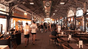 Ein überdachter Markt mit einer Uhr, Tischen, Stühlen und verschiedenen Geschäften.
