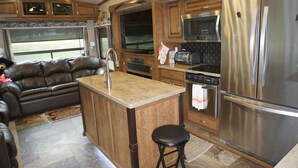 Cocina compacta para vehículos recreativos, con armarios de madera, electrodomésticos de acero inoxidable y una isla central.
