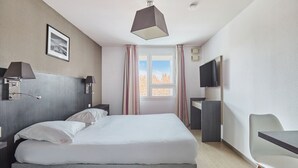 Ein Hotelzimmer mit Bett, Nachttischlampen, Fernseher, Schreibtisch und Stuhl.