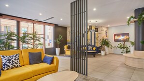Una hall moderna con un divano giallo, un tavolino rotondo e una reception.
