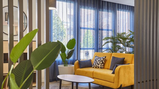 A modern living room with a yellow sofa, a round coffee table, and large green plants. - Studio au Centre, Climatisé + Équipé (Aix en Provence)