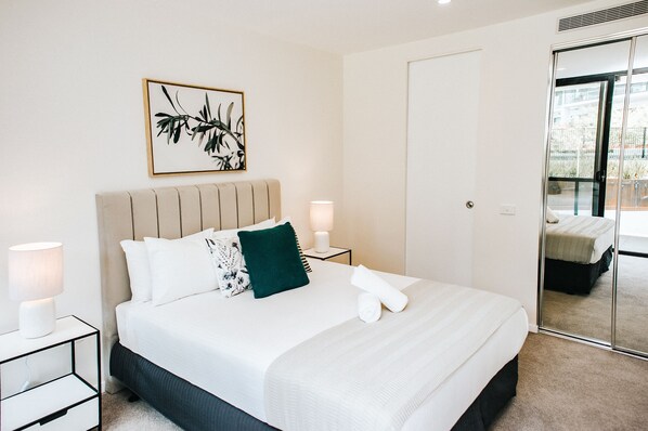 A neatly made bed with white bedding and a green pillow, a bedside lamp, and a framed artwork on the wall. - Kerridge St Apartments by Urban Rest (Kingston)