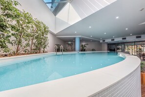 Piscina interna con vista sul cielo attraverso il soffitto, circondata da piante e arredamento moderno.