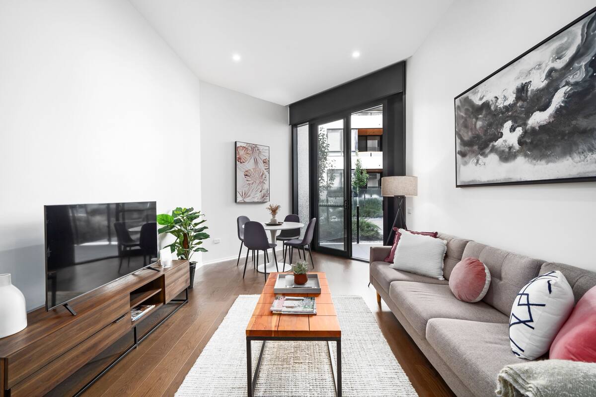 Ein modernes Wohnzimmer mit Flachbildfernseher, Couchtisch aus Holz und grauem Sofa mit dekorativen Kissen.