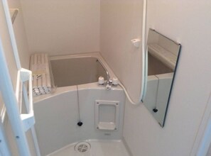 Pieni, valkoinen kylpyhuone, jossa on kylpyamme, wc ja peili.