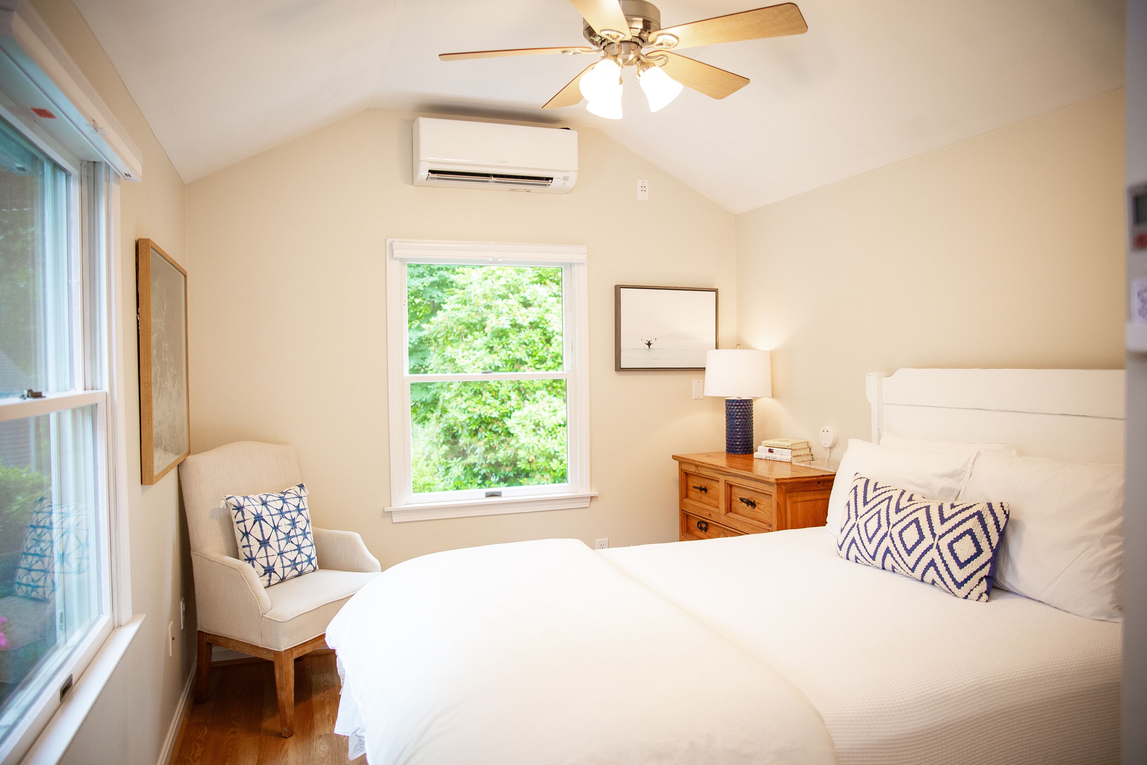 Quarto com cama, cadeira, mesa de cabeceira, janela e ventilador de teto.
