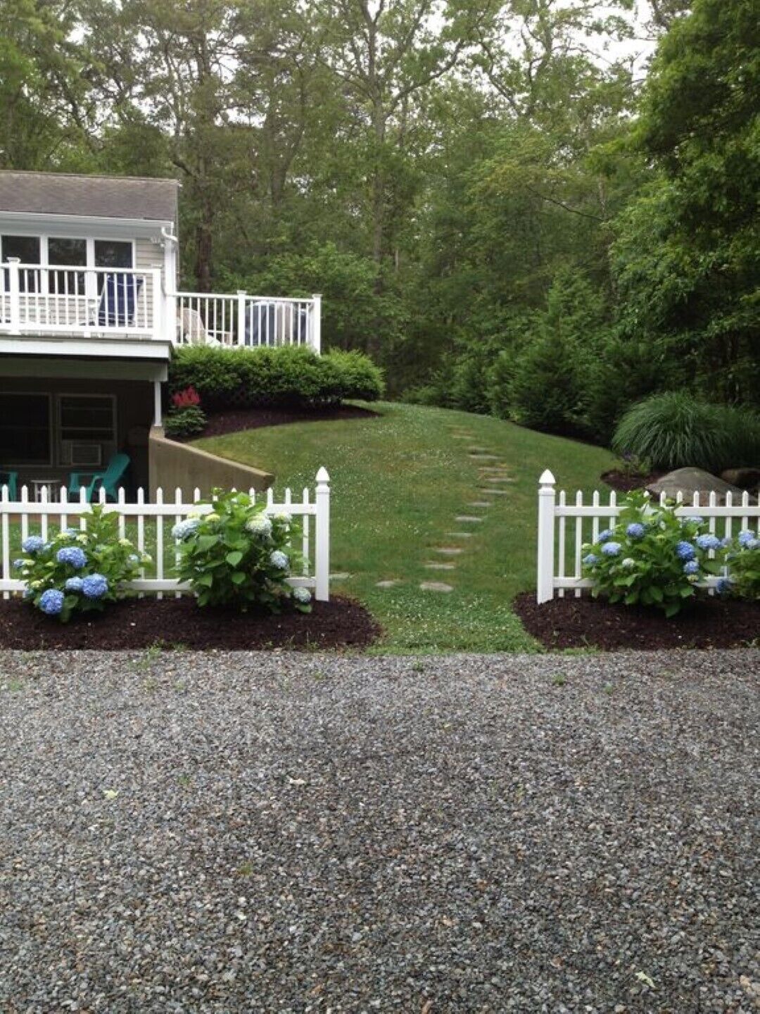 A house with a covered porch, a gravel driveway, and a well-maintained lawn.