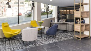 A modern lounge area with a large window, comfortable seating, a small table, and a bookshelf. - Studio Proche de la Sarthe, Accès Hammam (Le Mans)
