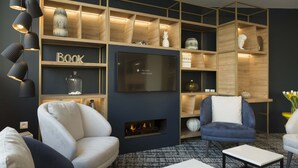 A modern living room with a fireplace, comfortable seating, and a large TV mounted on the wall. - Studio Proche de la Sarthe, Accès Hammam (Le Mans)