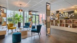 Moderni hotellin aula, jossa on vastaanottotiski, oleskelualue tuoleineen sekä suuri seinä, jossa on hotellin nimi.