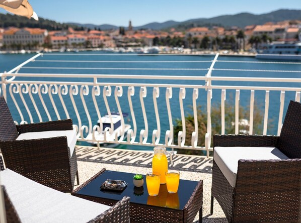 A balcony with wicker furniture, a table with drinks, and a view of a marina and cityscape.