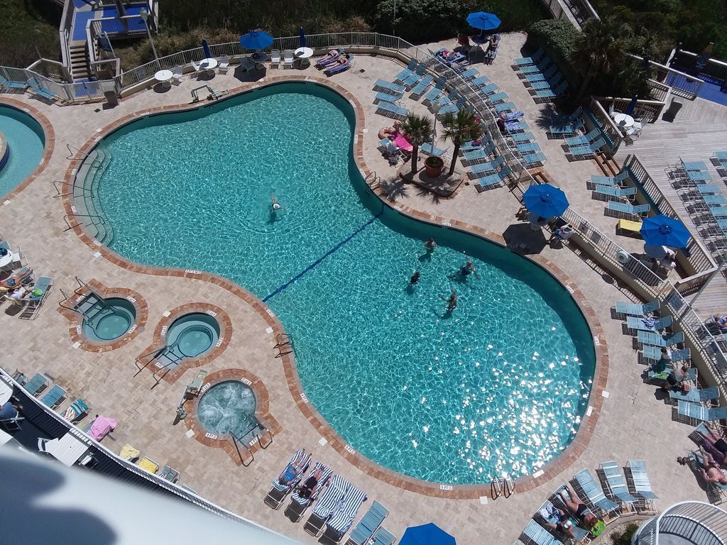 Une grande piscine extérieure divisée en plusieurs zones, entourée de chaises longues et de parasols.