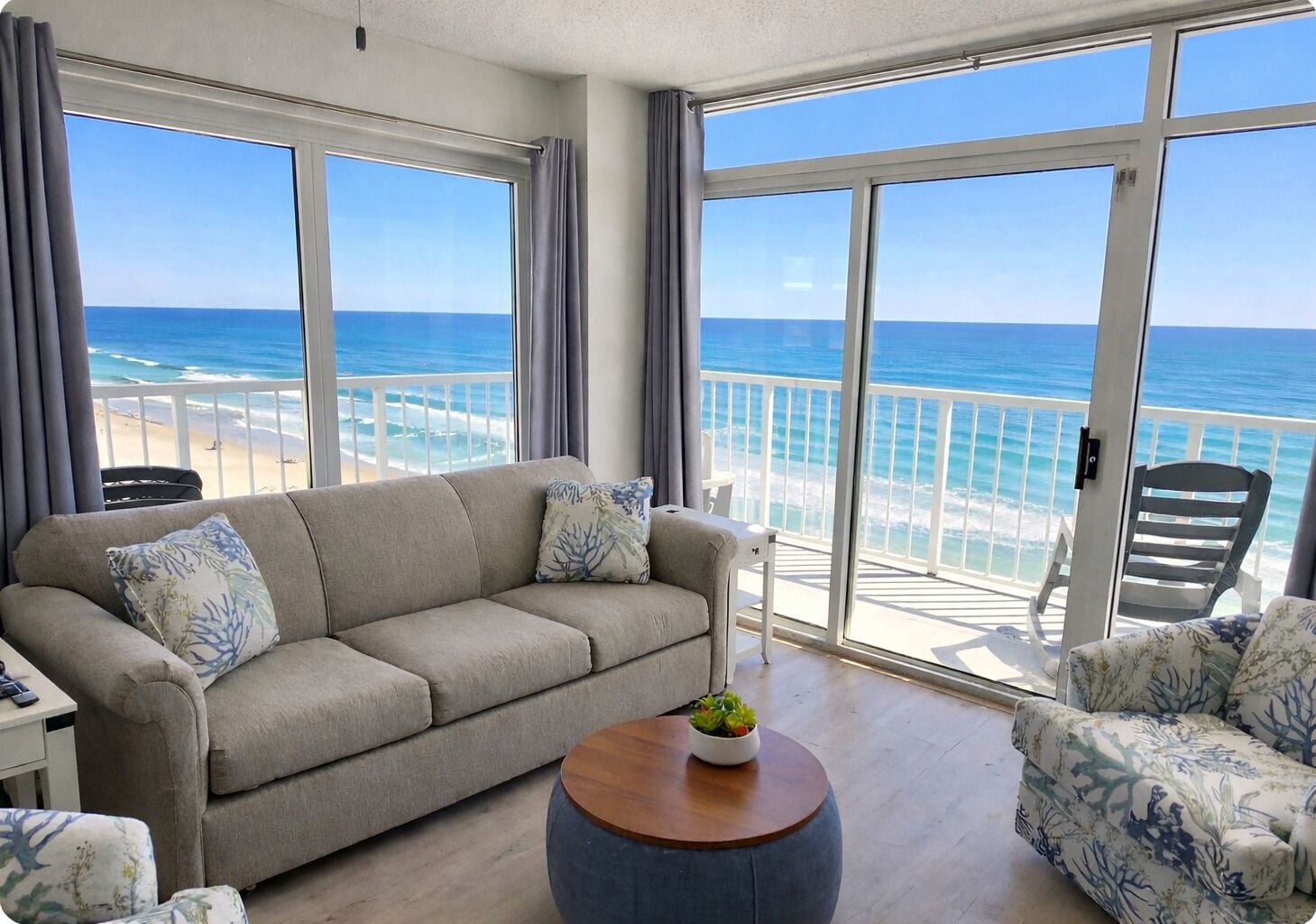 Un balcon avec vue sur l’océan, un canapé, un fauteuil et une petite table agrémentée d’une plante.