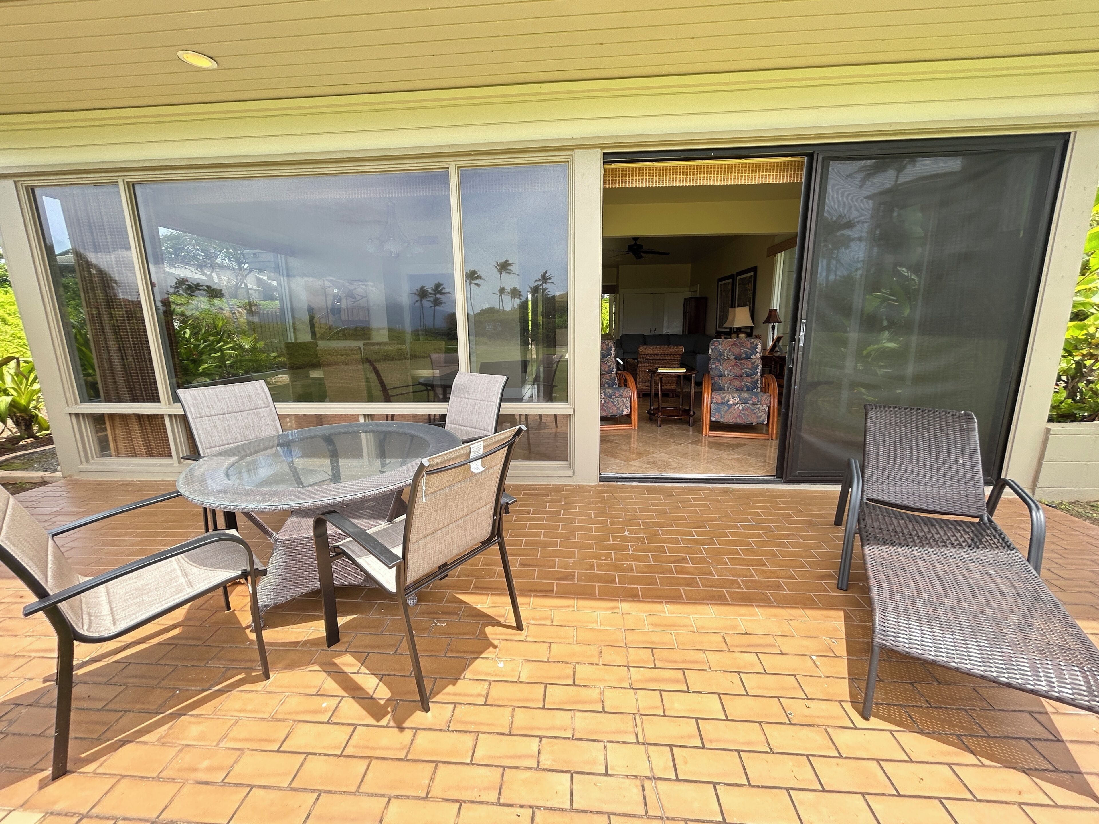Une terrasse extérieure avec une table et des chaises en verre, une porte-fenêtre coulissante donnant sur un espace intérieur et un sol en briques.