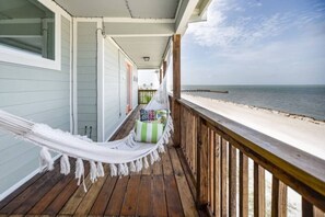 Une terrasse en bois avec un hamac, un petit coin salon avec des coussins et une vue sur la plage et l’océan.
