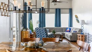 A modern living room with a dining area, a ceiling fan, and a large window with curtains. - SUNRISE ON MAG - Beach House (Port Lavaca)