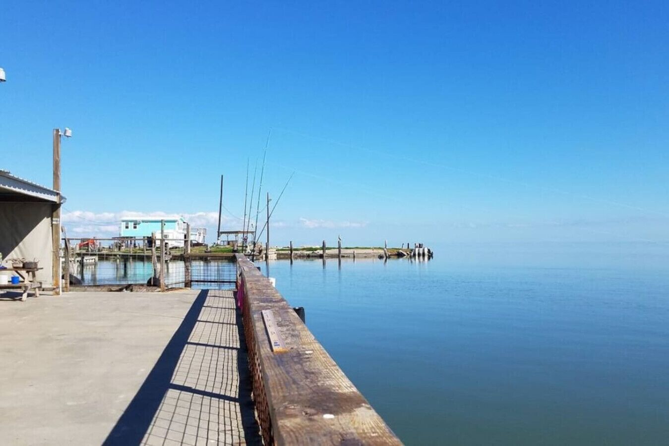 A pier extending into calm waters with a building on the left and a clear sky above.