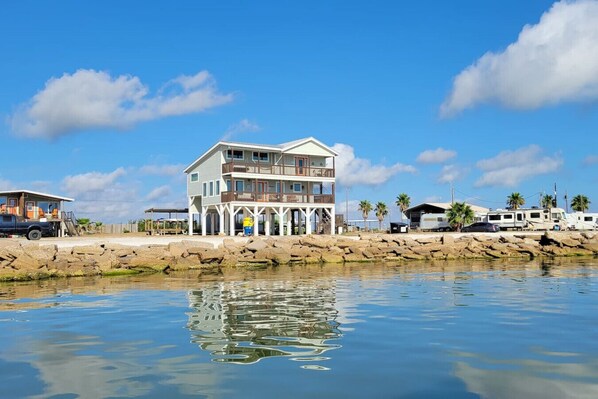 Une propriété en bord de mer, composée de plusieurs étages, avec un quai, des emplacements pour camping-cars et un ciel d’un bleu éclatant.