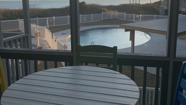 Een overdekt buitengebied met een zwembad, houten terras en uitzicht op het strand en de oceaan.