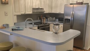 Een moderne keuken met witte kasten, een centraal kookeiland met barkrukken, een koelkast en een ingebouwde oven.