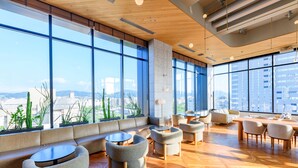 Un salón moderno con grandes ventanales, techo de madera y una variedad de asientos, incluyendo sofás y sillones.