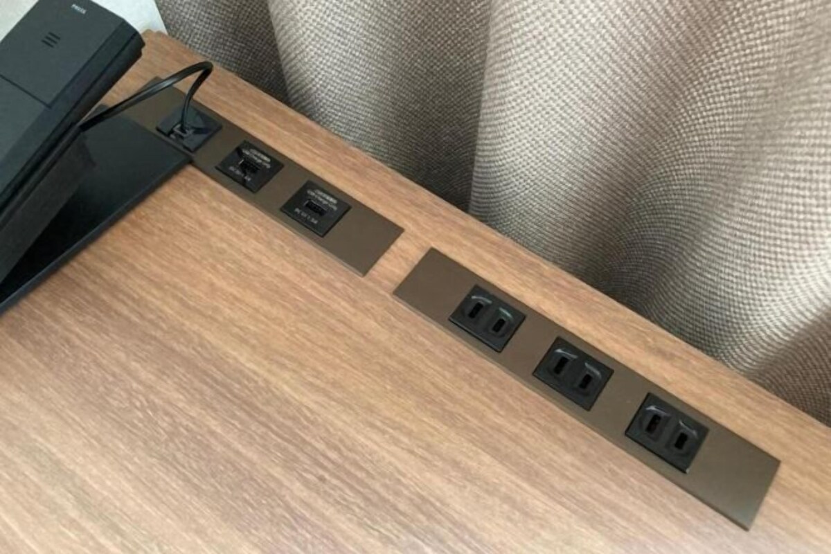 A wooden desk with a black printer and four electrical outlets.