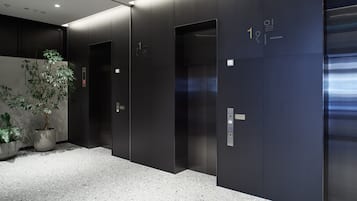 A modern elevator area with dark walls, a potted plant, and a speckled floor.