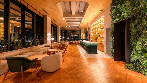 Un moderno vestíbulo de hotel con suelo de madera, zona de estar, bar y un jardín vertical cubierto de verde.