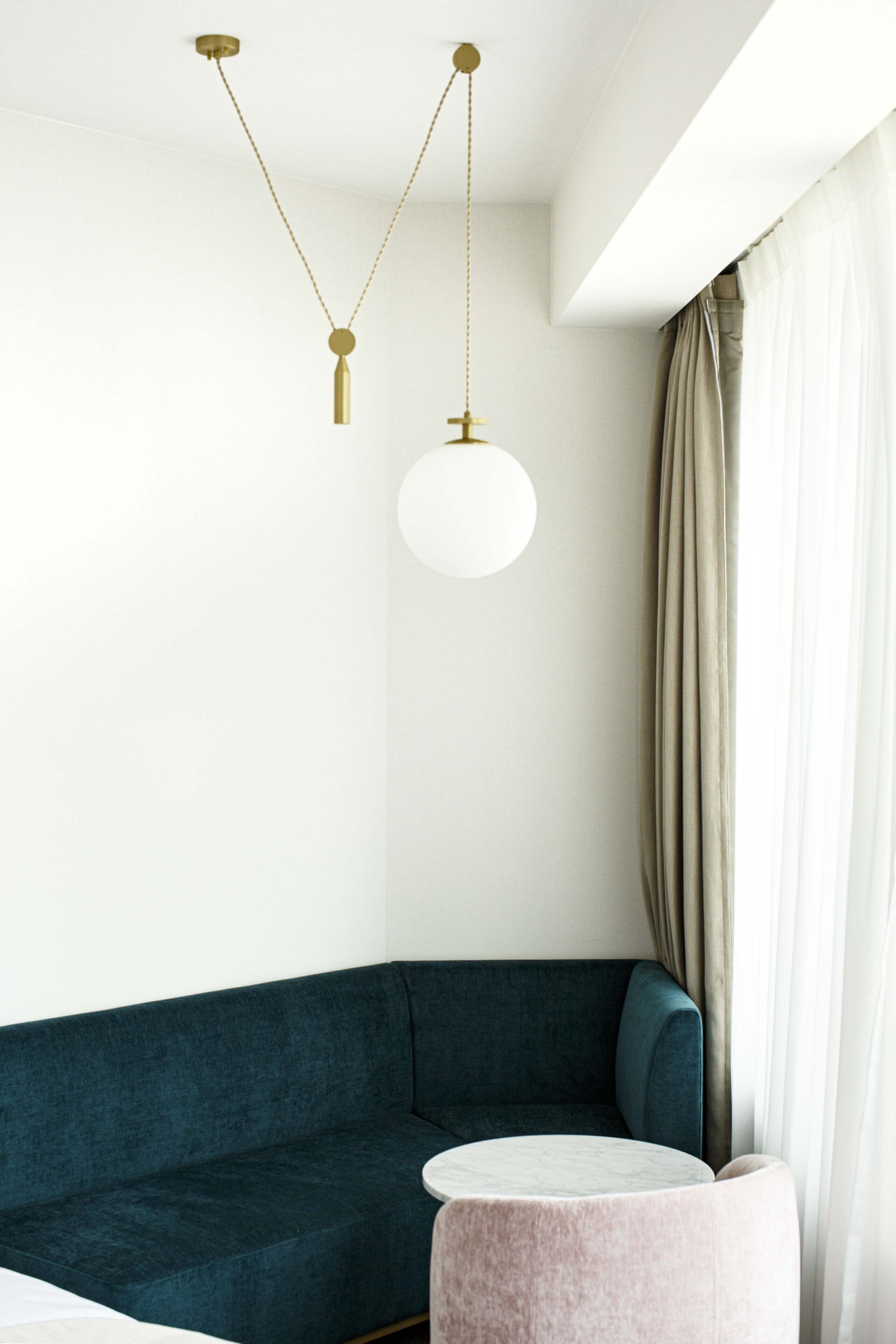 Ein modernes Zimmer mit einem petrolfarbenen Sofa, einem runden Tisch und einer Pendelleuchte.