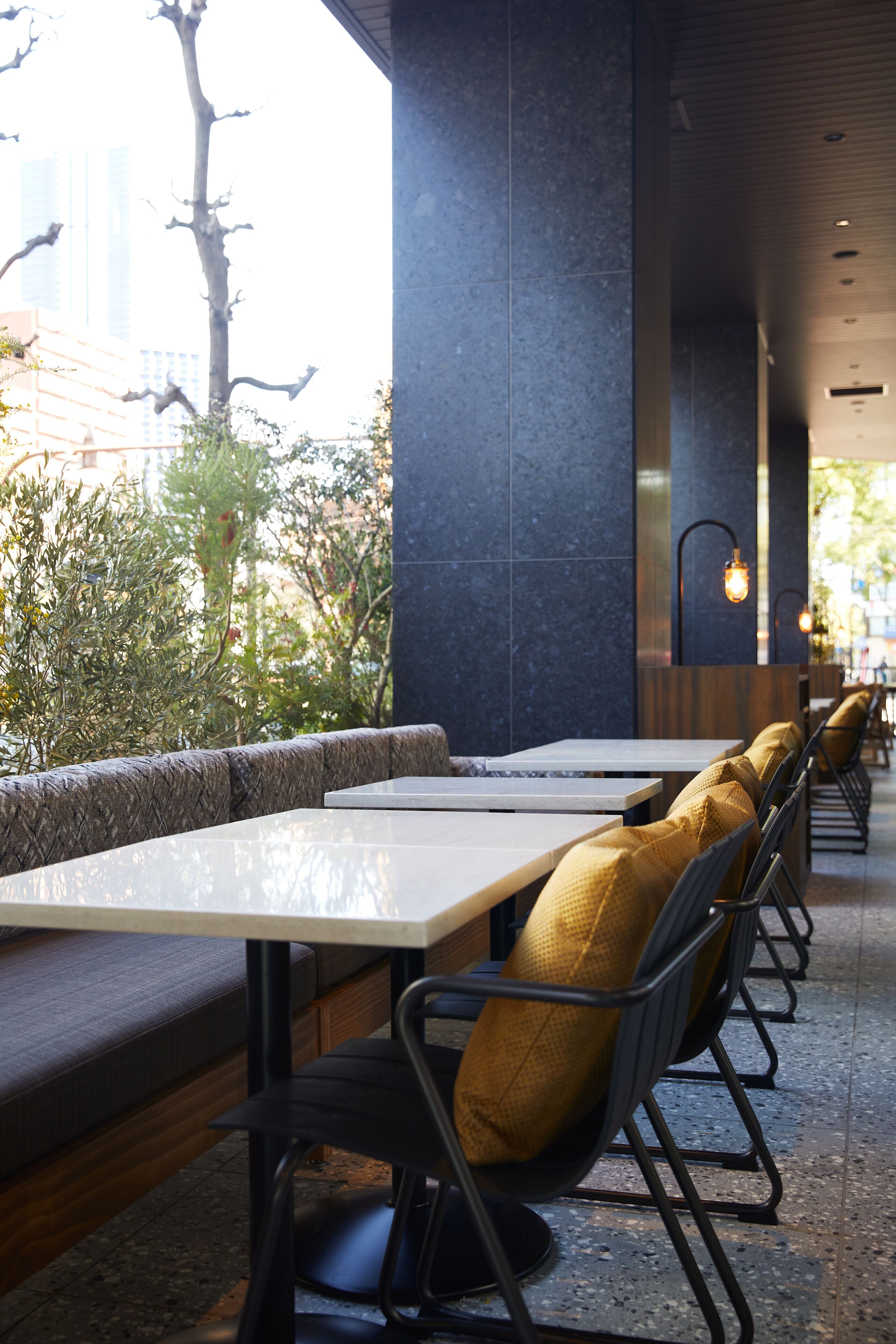 A restaurant with outdoor seating, dark interior walls, and a view of trees and buildings.
