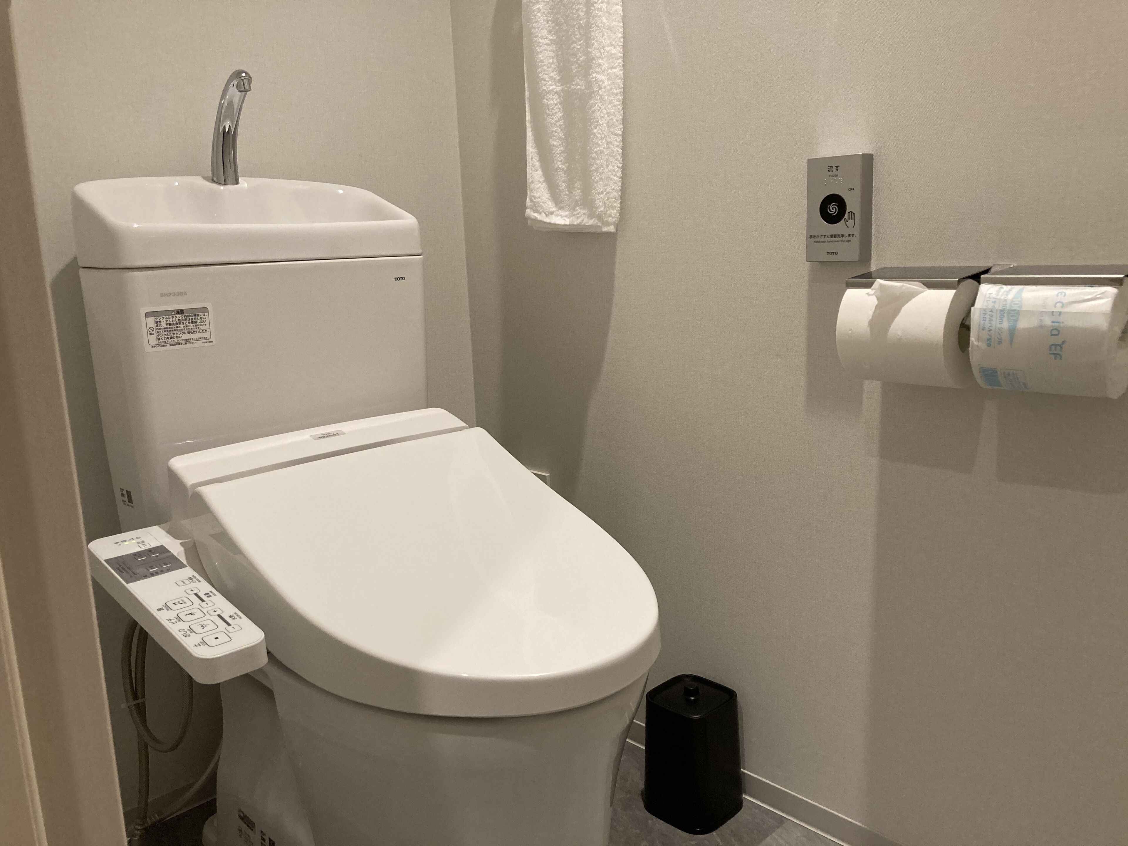 A modern bathroom with a toilet, a faucet, a control panel, a toilet paper holder, and a trash bin.