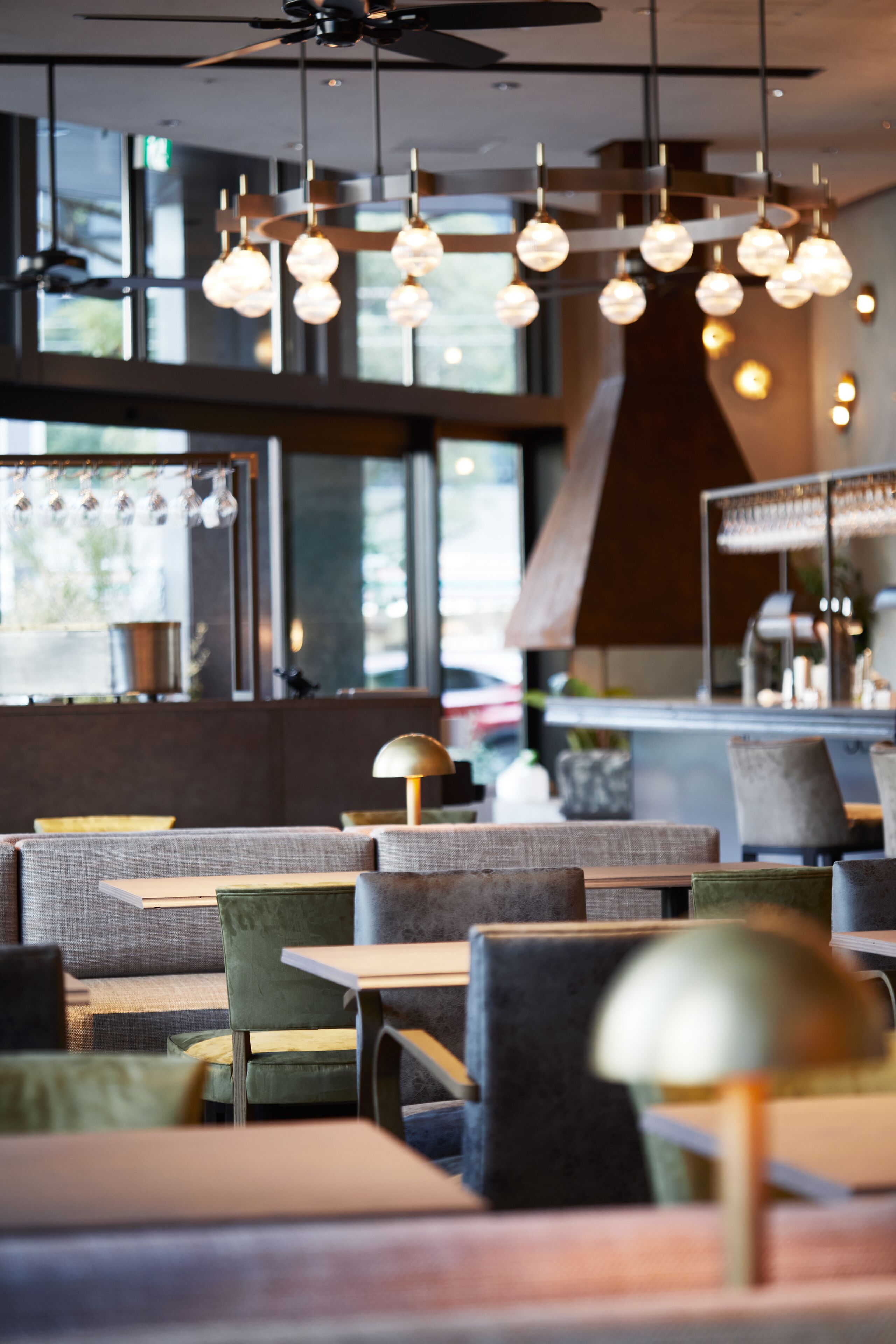 Un interior de restaurante moderno con mesas redondas, asientos acolchados, iluminación colgante y ventanas amplias.